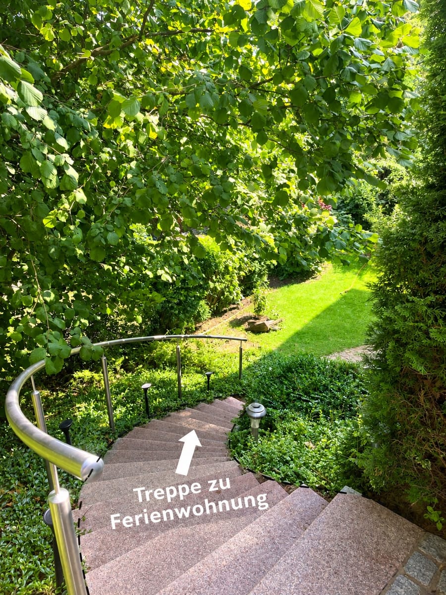 Gebogene Steintreppe mit Geländer, die in den Garten hinunterführt, mit der Aufschrift „Treppe zu Ferienwohnung“